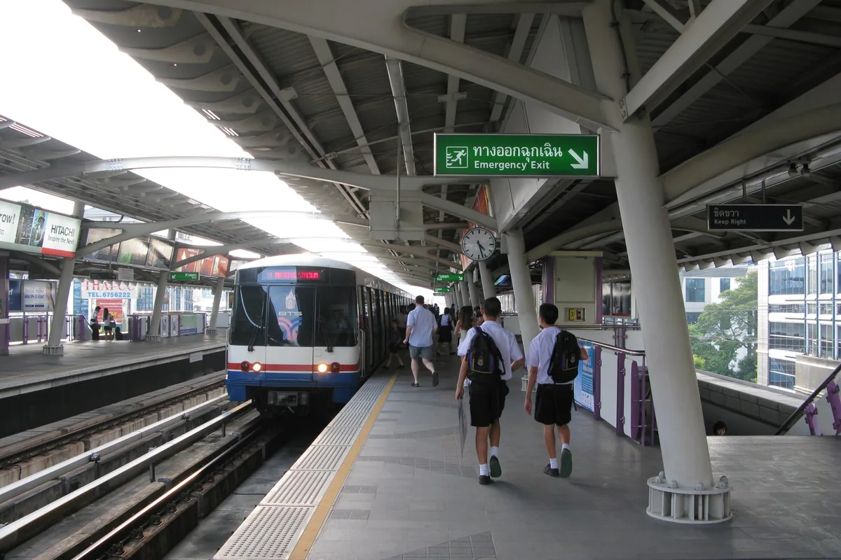 Passengers walking along an elevated BTS Skytrain platform in Bangkok as a train pulls into the station